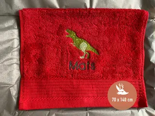 Kräftig rotes Handtuch mit grünem T-Rex-Dinosaurier-Stickmotiv von HeldenFaden. Eine spaßige und individuelle Geschenkidee für Kinder.