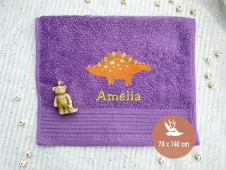 Lila Handtuch mit orangefarbenem Dinosaurier-Stickmotiv und Stacheldesign, hochwertig bestickt von HeldenFaden. Ideal für Kinder.