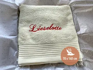 Beigefarbenes Handtuch mit roter personalisierter Bestickung von HeldenFaden. Weiches Material, ideal für Geschenke und individuelle Designs.