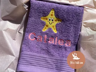 Lila Handtuch mit gelbem Seestern-Stickmotiv und rosa personalisierter Bestickung von HeldenFaden. Perfekt für den Alltag oder als individuelles Geschenk.