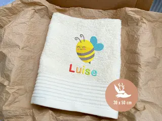 Ivory Cream farbenes Handtuch (30x50 cm) mit einer niedlichen Bienenstickerei und dem Namen 'Luise', der in Regenbogenfarben gestickt ist. Perfekt als Geschenk für Kinder.