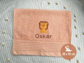 Handtuch in der Farbe Salmon (30x50 cm) mit einer süßen Löwenstickerei und dem Namen 'Oskar', gestickt in passenden braunen Tönen. Perfekt als personalisiertes Geschenk für Kinder.