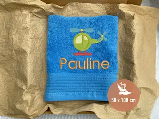 Aqua Azures Handtuch mit grünem Hubschrauber-Stickmotiv und dem Namen „Pauline“ in orangener Schrift. Perfektes Kinderhandtuch (50x100 cm) von HeldenFaden.