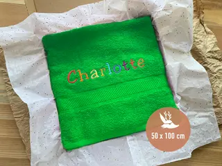 Grünes Handtuch (50x100 cm) mit buntem Schriftzug „Charlotte“. Perfektes personalisiertes Geschenk von HeldenFaden für besondere Anlässe.