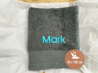 Graues Handtuch (50x100 cm) mit dem Namen „Mark“ in türkisfarbener Schrift. Schlichtes und hochwertiges Handtuch von HeldenFaden für individuelle Bestickungen.