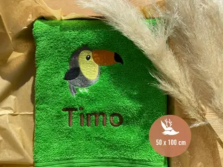 Grünes Handtuch (50x100 cm) mit Tukan-Stickmotiv und dem Namen „Timo“ in brauner Schrift. Perfektes personalisiertes Handtuch für Tierliebhaber von HeldenFaden.